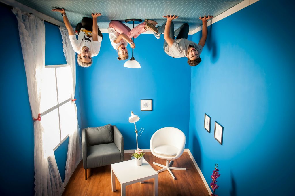 의자, 테이블, 액자 사진 등 반전 가구가 놓인 파란색 방에 사람들이 거꾸로 매달려 있는 것처럼 보입니다.