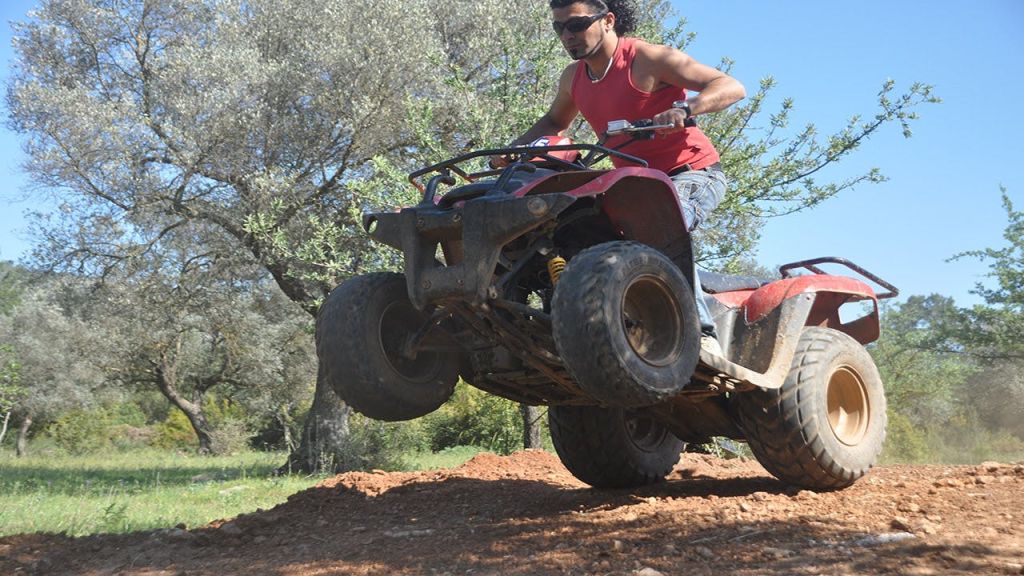 나무를 배경으로 공중에서 ATV를 몰고 흙길을 지나가는 빨간색 탱크탑의 사람.