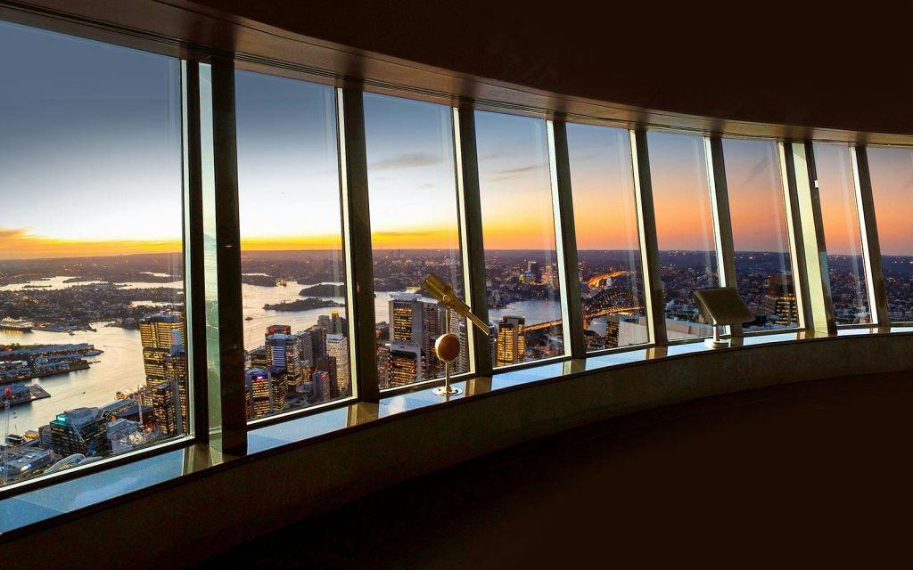 높은 창문을 통해 바라보는 석양을 배경으로 도시 스카이라인과 항구 전망을 감상할 수 있으며, 전경 전망대에는 망원경이 설치되어 있습니다.