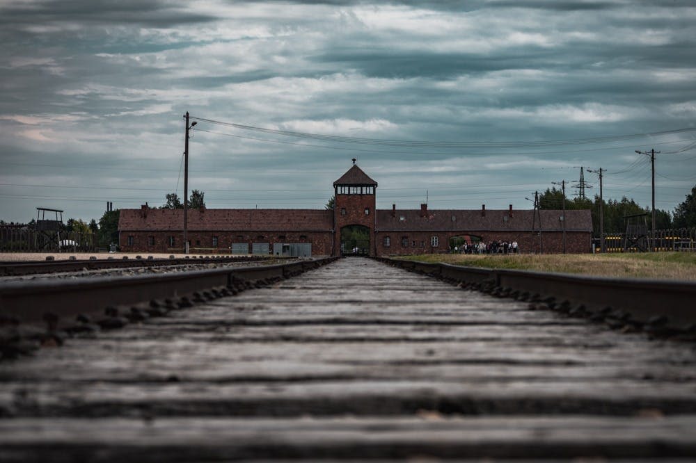탁한 하늘 아래 중앙 출입구 타워가 있는 벽돌 건물로 이어지는 목조 철길.