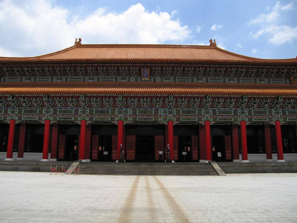 화려한 디테일, 빨간색 기둥, 타일로 마감된 지붕이 있는 대형 전통 건물입니다. 계단이 넓으면 입구로 연결됩니다. 위의 맑은 하늘.