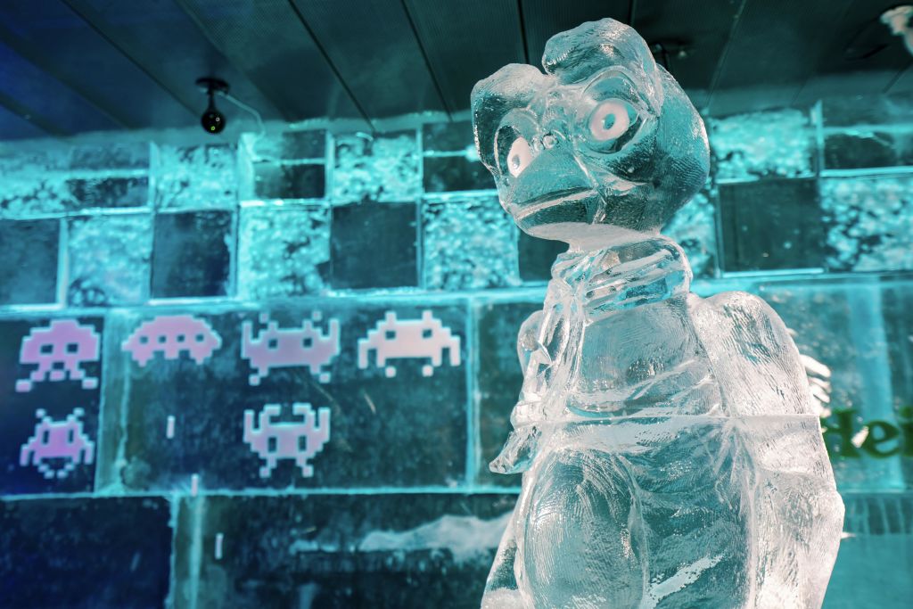 픽셀 아트 피규어와 파란색 조명이 있는 벽 앞에 커다란 눈을 가진 캐릭터의 얼음 조각.