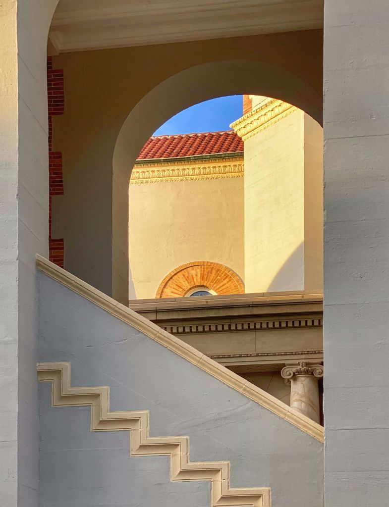 맑고 푸른 하늘을 배경으로 아치, 기둥, 계단과 따뜻한 조명이 특징인 건축물입니다.