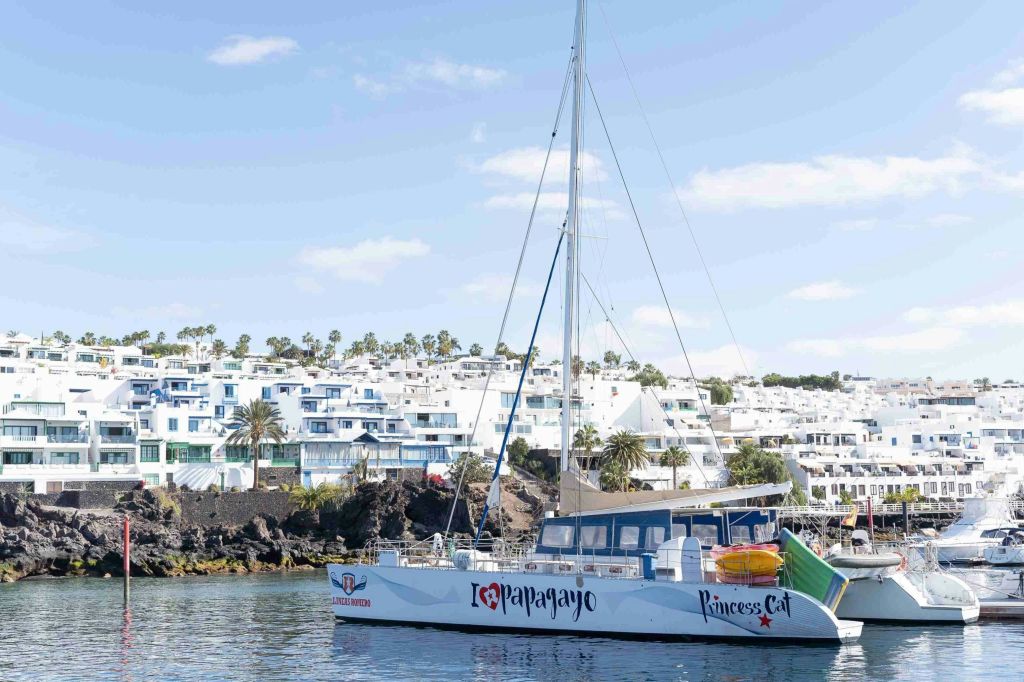 하얀 건물과 야자수가 있는 해안 마을 근처에 "I ❤️ Papagayo" 와 "Princess Cat" 이 있는 쌍동선이 정박해 있습니다.