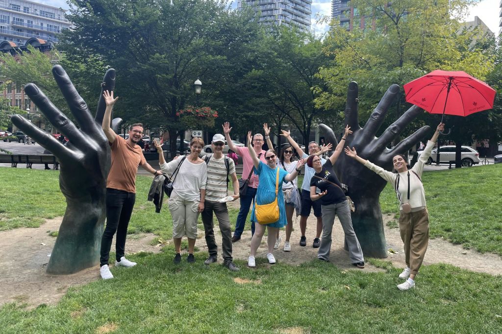 공원에서 나무와 건물을 배경으로 커다란 손조각을 들고 포즈를 취하는 사람들.