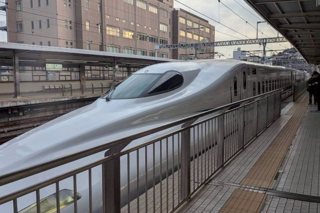 세련된 은색 탄환 열차가 현대식 건물을 배경으로 역 플랫폼에 정차했습니다.