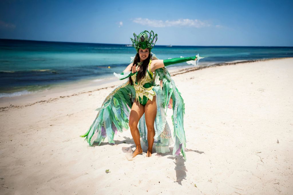 정교한 녹색 의상을 입은 사람이 화창한 하늘 아래 바다를 배경으로 모래 해변에서 포즈를 취하고 있습니다.