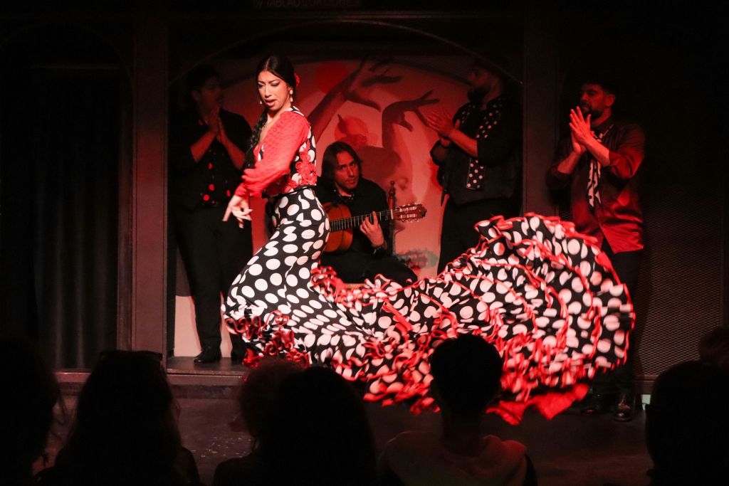 빨간색과 검은색 폴카 도트 드레스를 입은 플라멩코 댄서가 무대에서 기타를 연주하는 뮤지션들과 함께 공연합니다.