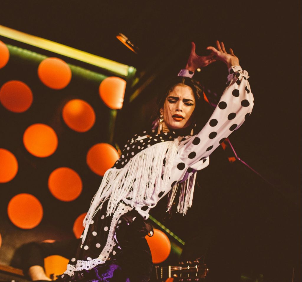 댄서는 커다란 주황색 점이 특징인 배경을 배경으로 물방울 무늬의 의상을 입고 열정적으로 공연합니다.