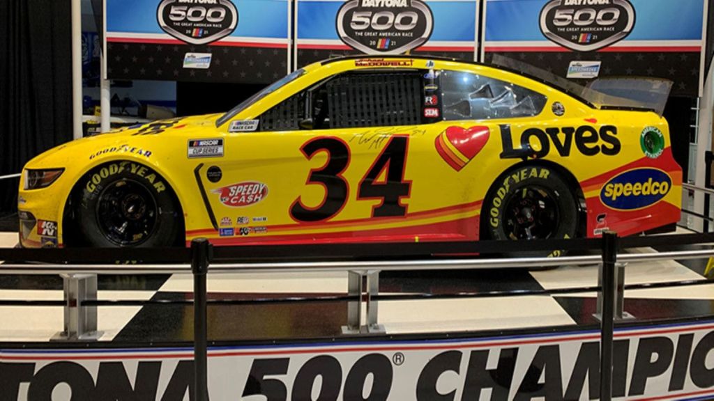 숫자 34와 사랑의 로고가 새겨진 노란색과 빨간색 레이스카가 Daytona 500 이벤트에 전시되어 있습니다.