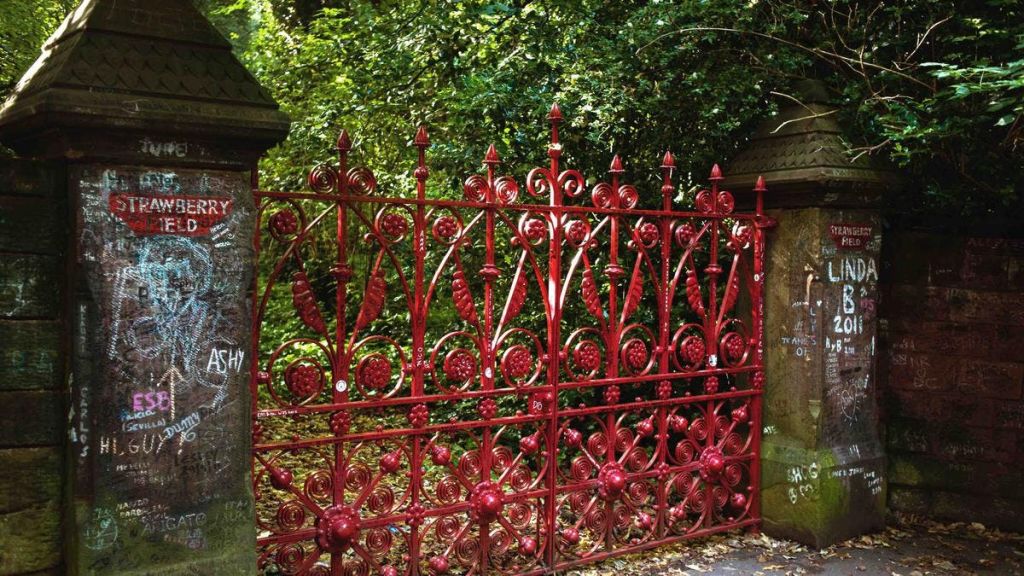 빽빽한 녹지로 둘러싸인 돌기둥 사이에 세워진 정교한 패턴의 화려한 붉은 연철 게이트.