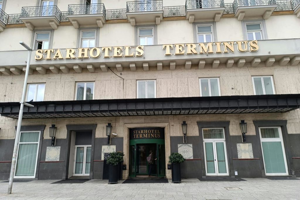 커다란 창문과 화분에 둘러싸인 중앙 출입구가 있는 스타호텔 종착역의 외관으로, 발코니가 있는 베이지색 건물 아래에 자리하고 있습니다.