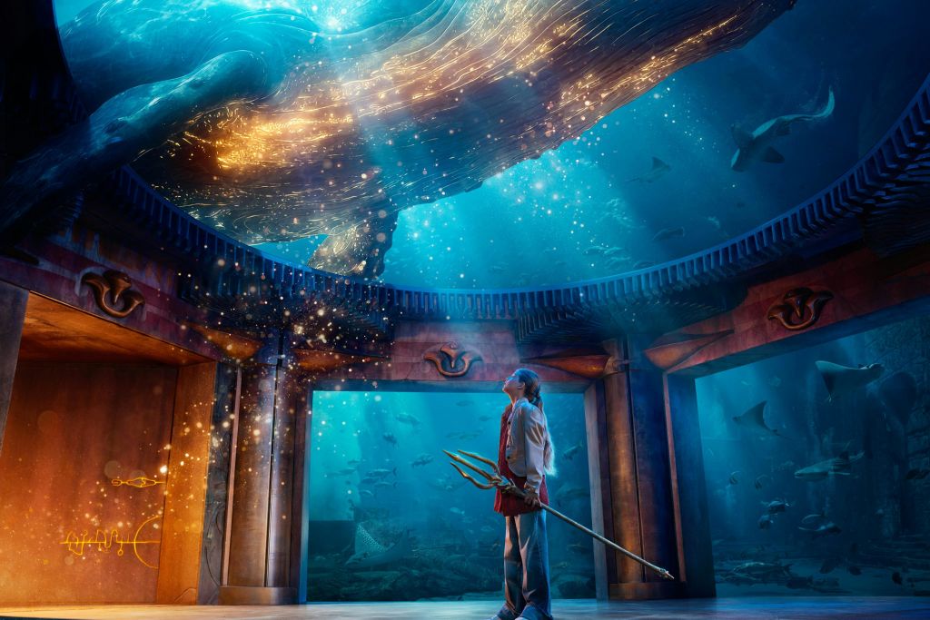 삼지창을 들고 있는 한 사람이 수중에서 빛나는 바다 생물을 배경으로 서 있습니다.