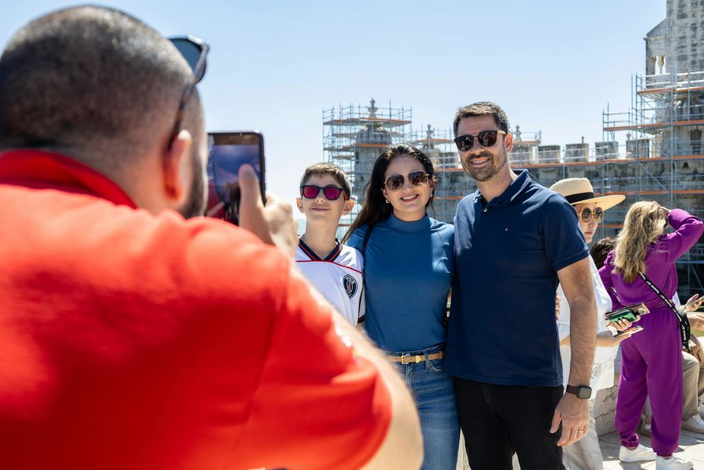 빨간 셔츠를 입은 사람이 공사 현장을 배경으로 카메라를 보며 웃고 있는 일행의 사진을 찍고 있습니다.