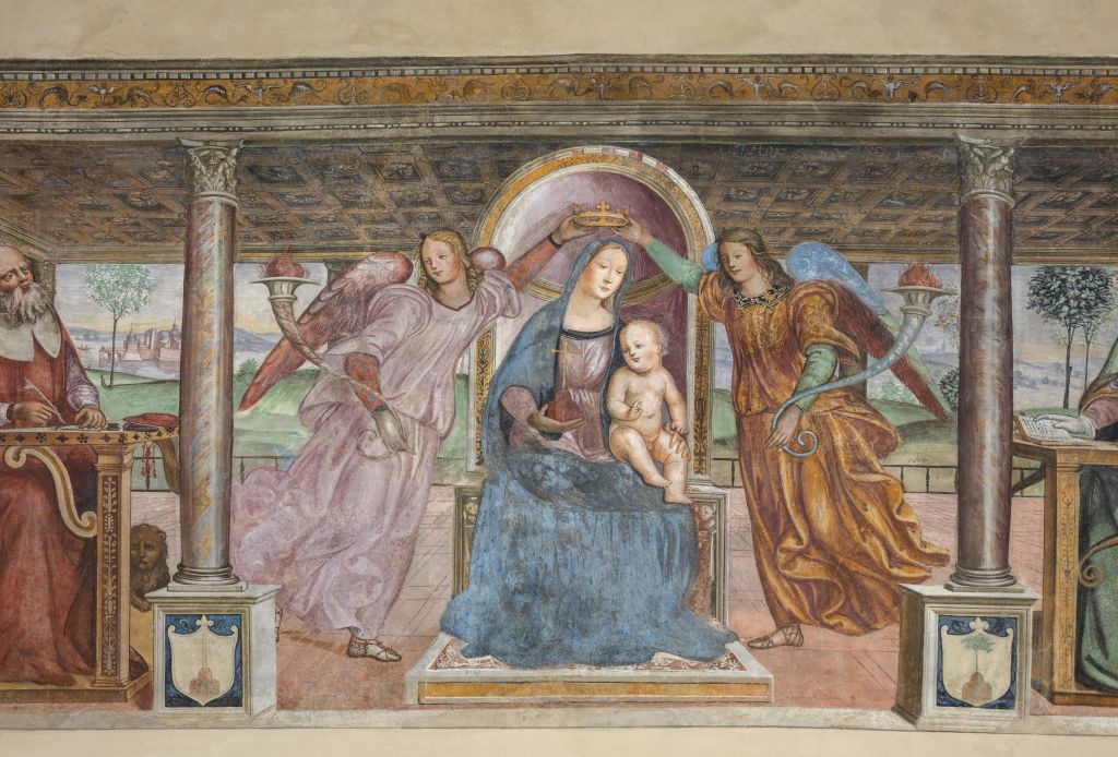 무릎에 아이를 안고 앉아 있는 한 여성이 장식 천장 아래 두 천사의 관을 쓰고 있습니다.