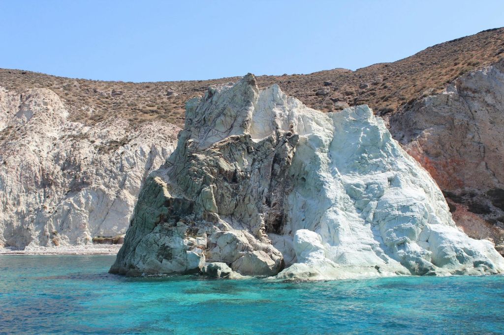 청명한 청록색 바다로 둘러싸인 바위 노두와 맑고 푸른 하늘 아래 언덕길을 배경으로 황량한 언덕길이 펼쳐집니다.