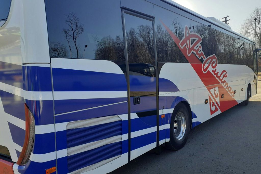 파란색과 흰색 줄무늬가 있는 주차된 버스의 측면 모습과 측면에 빨간색 텍스트가 있습니다. 나무는 배경에 있습니다.