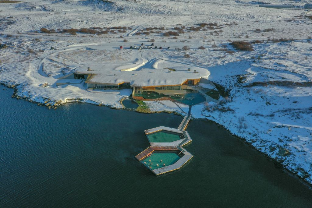 눈으로 둘러싸인 현대적인 건물과 호수에 인접한 지열 수영장 단지의 공중 전망.