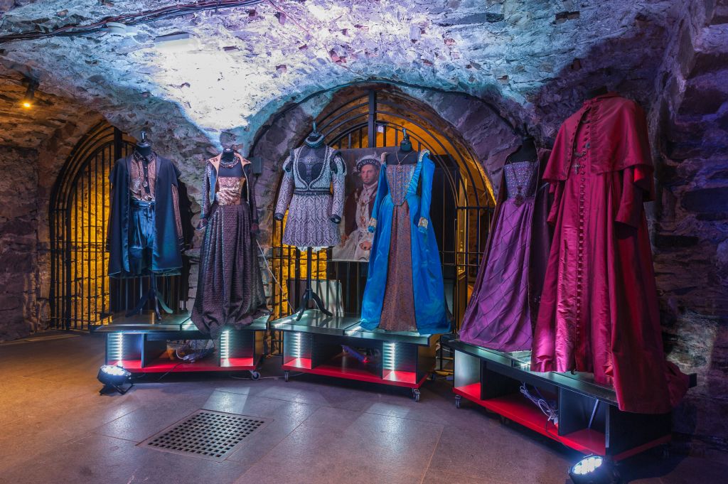 마네킹은 아치형 출입구와 철조망을 배경으로 조명이 어두운 석실에 화려한 역사 의상을 전시합니다.