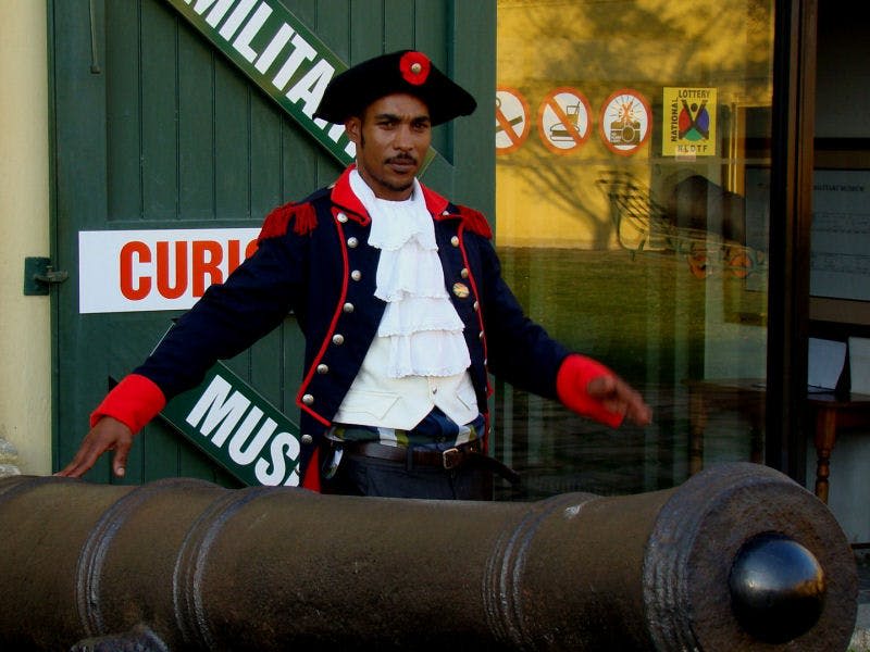 박물관 표지판을 배경으로 대포 옆에 서 있는 역사적인 군복을 입은 사람.