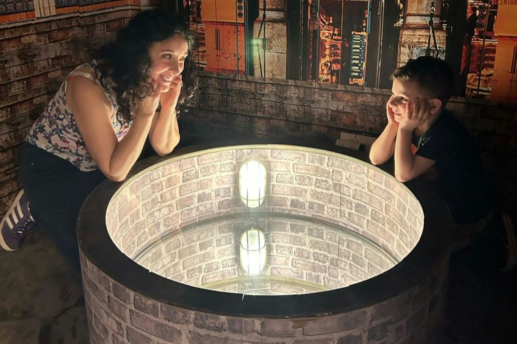 한 소년이 원형으로 조명이 잘 비춰진 구조물에 앉아 장식용 벽을 배경으로 턱을 손에 얹고 있습니다.