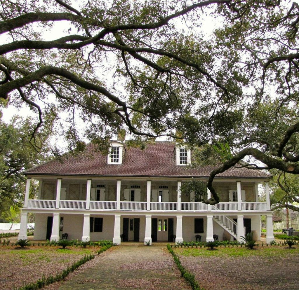 나뭇가지가 펼쳐진 커다란 참나무로 둘러싸인 넓은 현관이 있는 유서 깊은 2층짜리 하얀 집입니다.