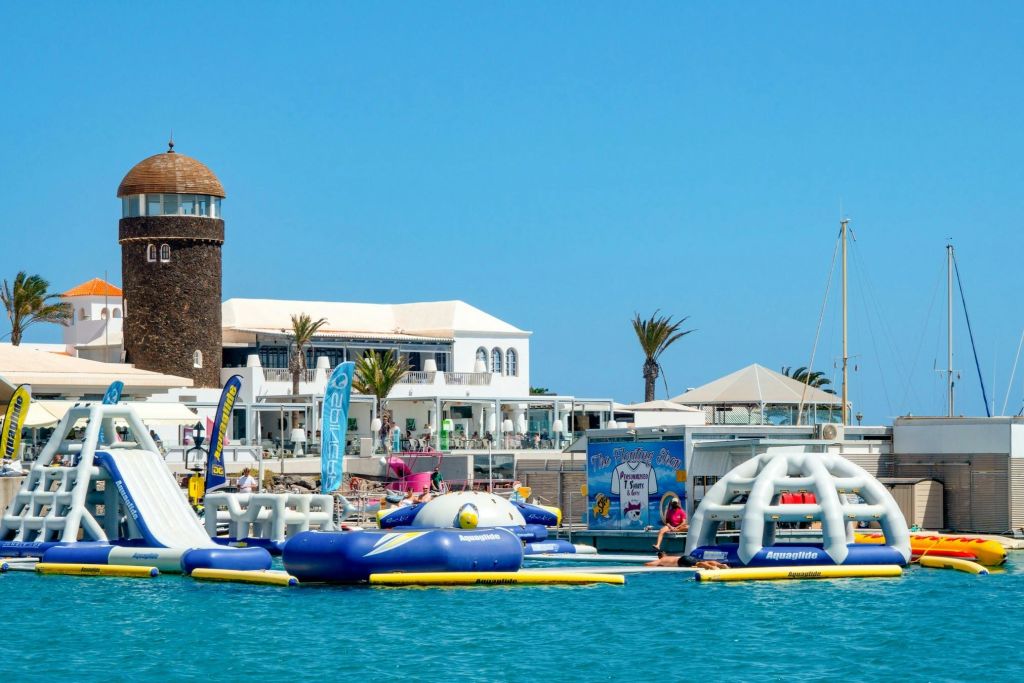 해안 건물 앞에 팽창식 구조물과 밝고 푸른 하늘 아래 야자수가 있는 수상 워터파크.