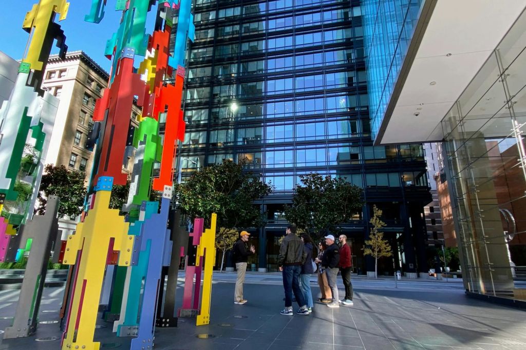 현대적인 유리 건물을 배경으로 도시 광장의 화려한 추상 조형물 근처에 사람들이 서 있습니다.