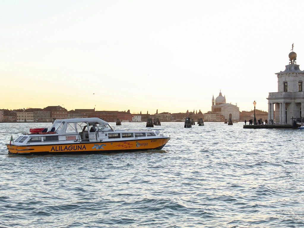 역사적인 건물과 교회 돔을 배경으로 '알릴라구나' 라는 이름의 수상 택시가 운하를 가로지르고 있습니다.