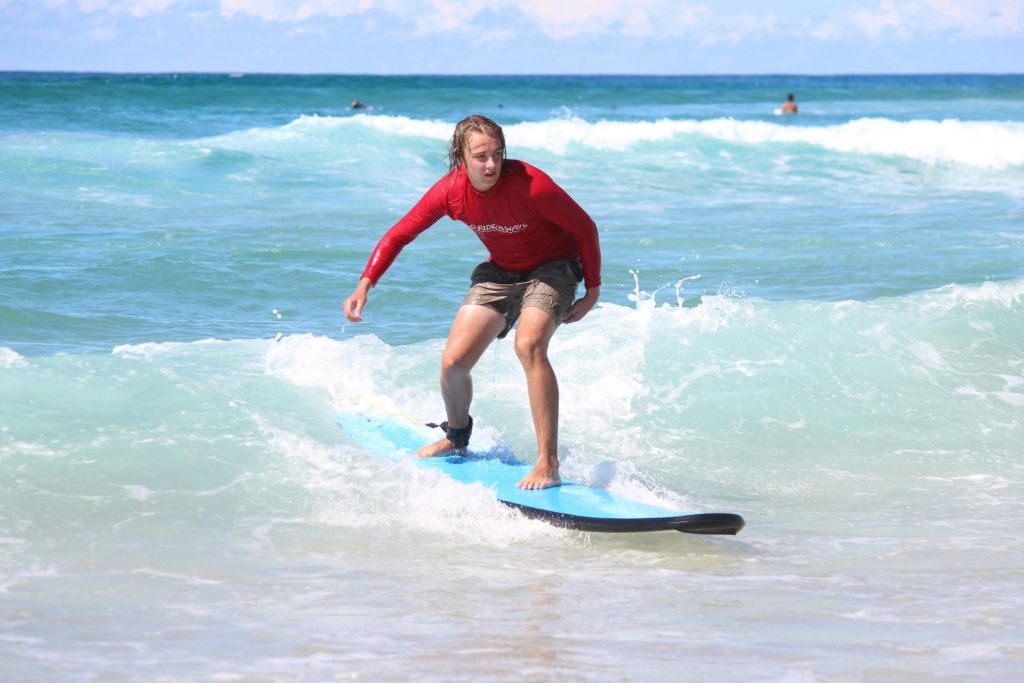 빨간색 발진 가드와 반바지를 입은 사람이 파란색 파도에서 서핑을 하고 있으며, 다른 서퍼들도 서핑을 하고 있습니다.