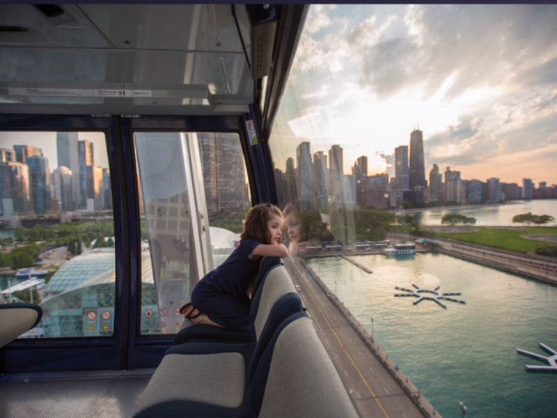 한 어린이가 도시의 스카이라인과 해질녘 바닷가에서 움직이는 오두막의 창문을 내다보고 있습니다.