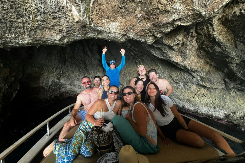 10명의 일행이 바위 동굴 안에서 보트를 타고 미소를 짓고 포즈를 취하고 있습니다. 한 사람이 팔을 들어 올렸습니다.