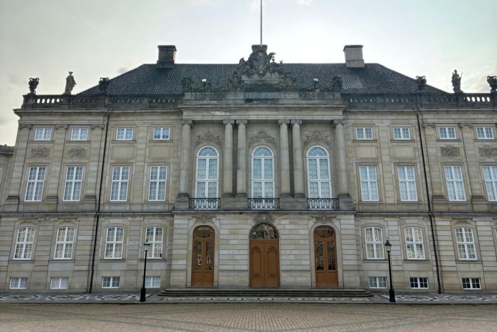 대칭적인 건축물, 커다란 창문, 화려한 디테일, 두 개의 나무 문이 흐린 하늘 아래 보이는 역사적인 건물.