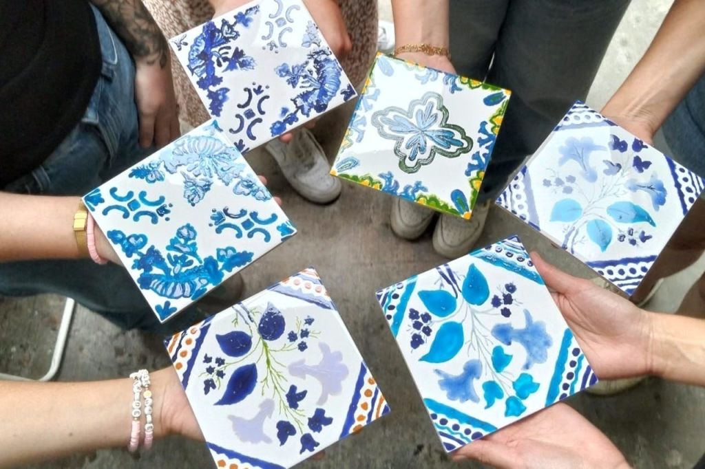 꽃무늬와 기하학적 디자인이 돋보이는 화려한 수제 타일을 들고 있는 사람들로, 콘크리트를 배경으로 위에서 바라본 모습입니다.