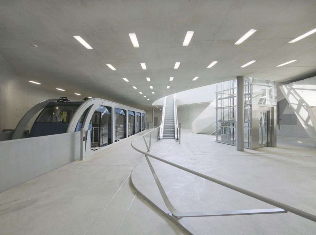 밝은 천장 조명 아래 매끄러운 유리벽 열차, 에스컬레이터, 유리 엘리베이터가 있는 현대적인 기차역 내부.