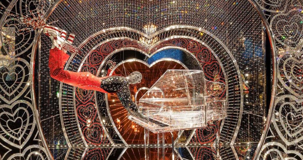 투명한 피아노를 연주하는 마네킹으로, 하트 모양과 반짝이는 조명이 특징인 장식용 배경에 세팅되어 있습니다.