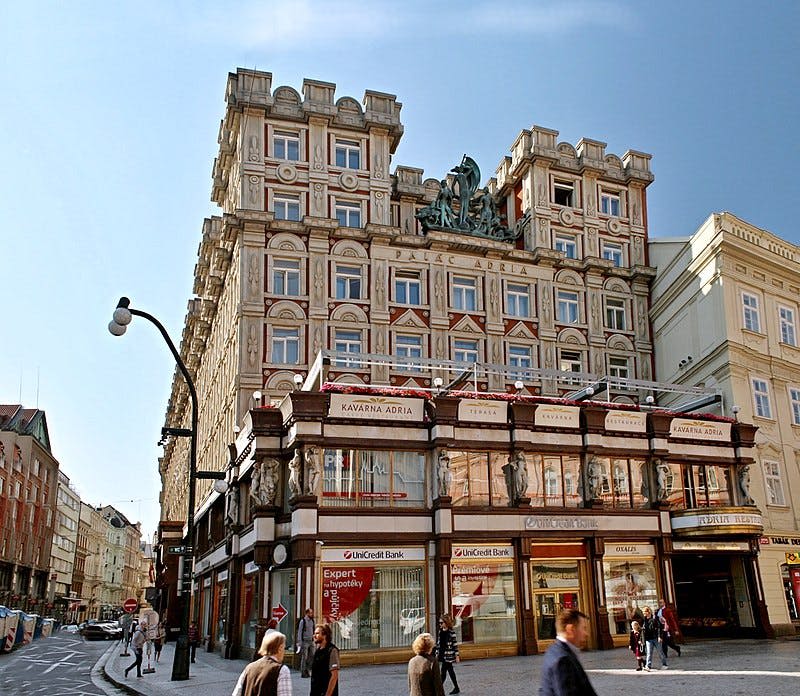 유니크레딧 뱅크 (UniCredit Bank) 를 포함한 1층 상점이 있는 화려한 복층 건물. 사람들은 앞길을 걷습니다. 맑고 푸른 하늘.