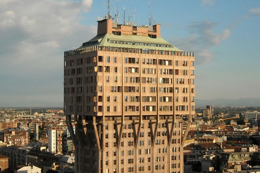 도시 경관을 배경으로 좁은 지지대, 창문, 안테나가 특징인 독특한 건축 디자인의 높은 베이지색 건물.