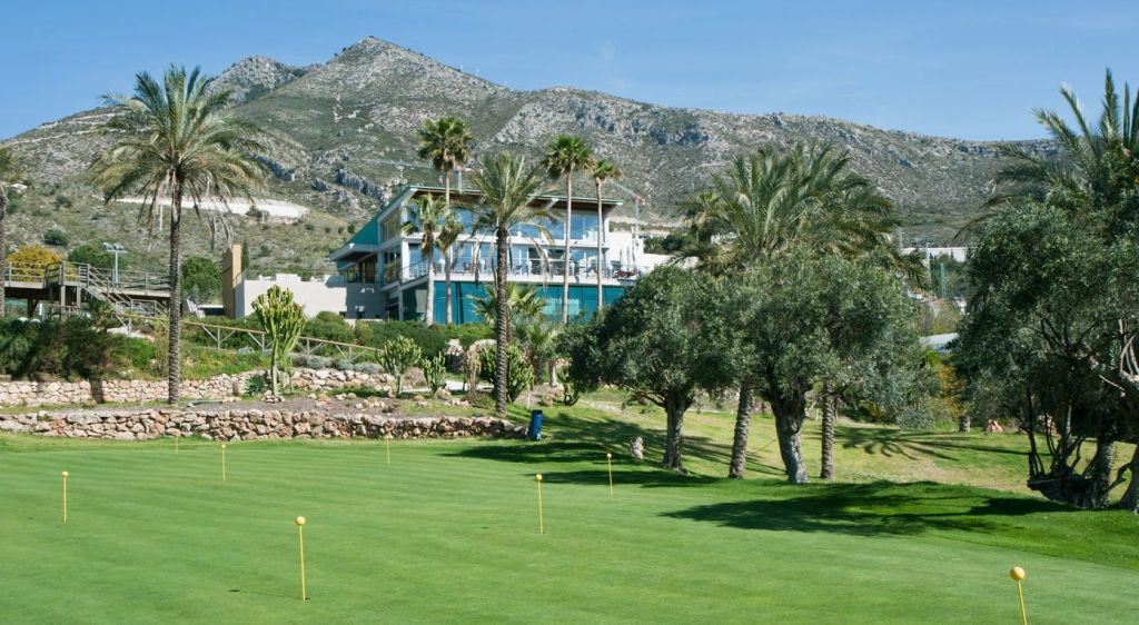 야자수와 녹지로 둘러싸인 현대적인 건물로, 산악 지역에 위치해 있으며 전경에 잘 손질된 잔디밭이 있습니다.