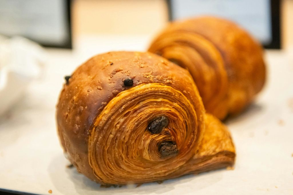 크루아상 롤을 닮은 황금빛 각질의 질감과 초콜릿 조각이 들어간 구운 페이스트리를 클로즈업합니다.