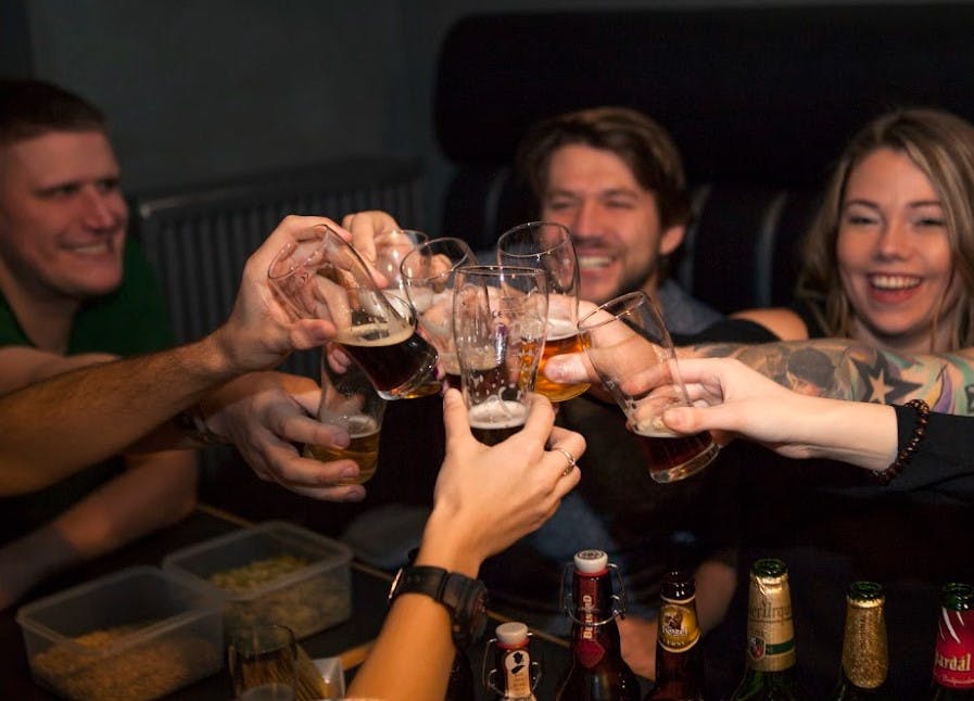 한 무리의 사람들이 웃으며 맥주잔을 찰칵거리며 앞에 놓인 테이블에 병을 들고 있습니다.