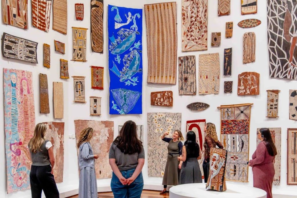 갤러리 벽에 전시된 다채로운 토착 예술 작품을 감상하는 사람들.