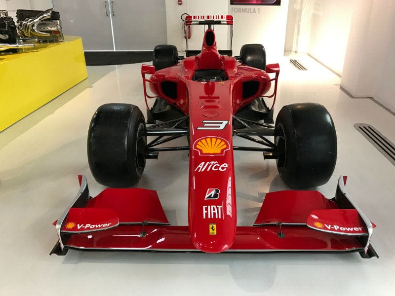 다양한 스폰서 로고가 있는 레드 포뮬러 1 레이싱 카는 광택이 있는 흰색 바닥에 실내에 전시되어 있습니다.