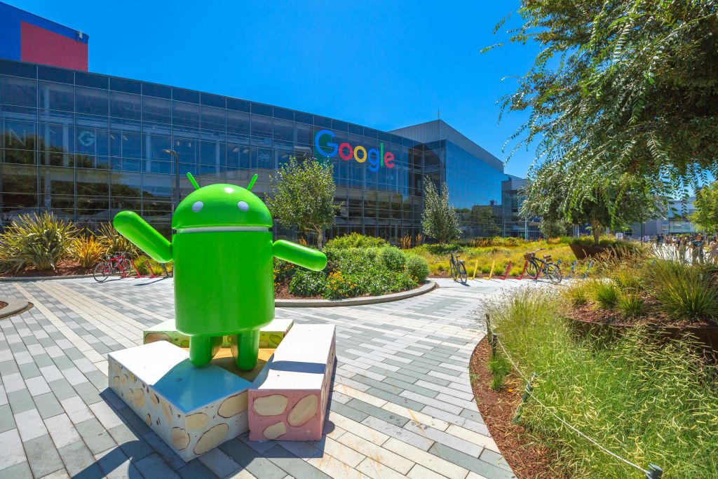 울창한 조경과 자전거로 둘러싸인 커다란 "Google" 로고가 있는 Google 본사 건물 앞의 녹색 Android 동상.