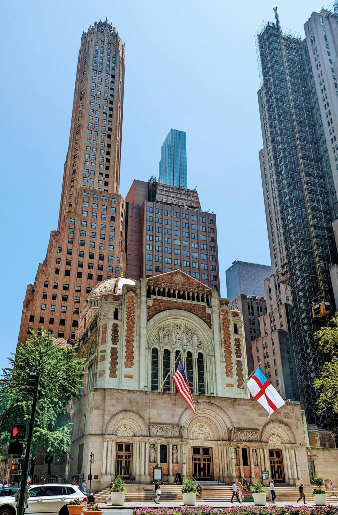 현대적인 고층 건물로 둘러싸인 미국 국기와 십자가 깃발이 있는 역사적인 건축물입니다.