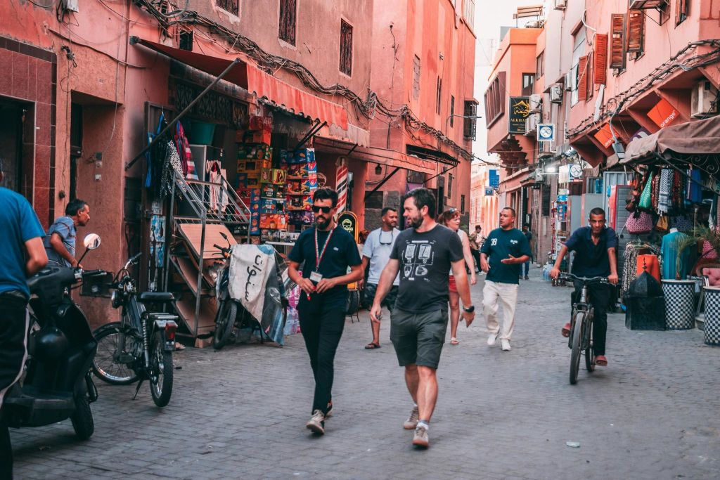 도심 속 다채로운 상점과 건물이 늘어선 좁고 번화한 거리를 걷고 자전거를 타는 사람들.