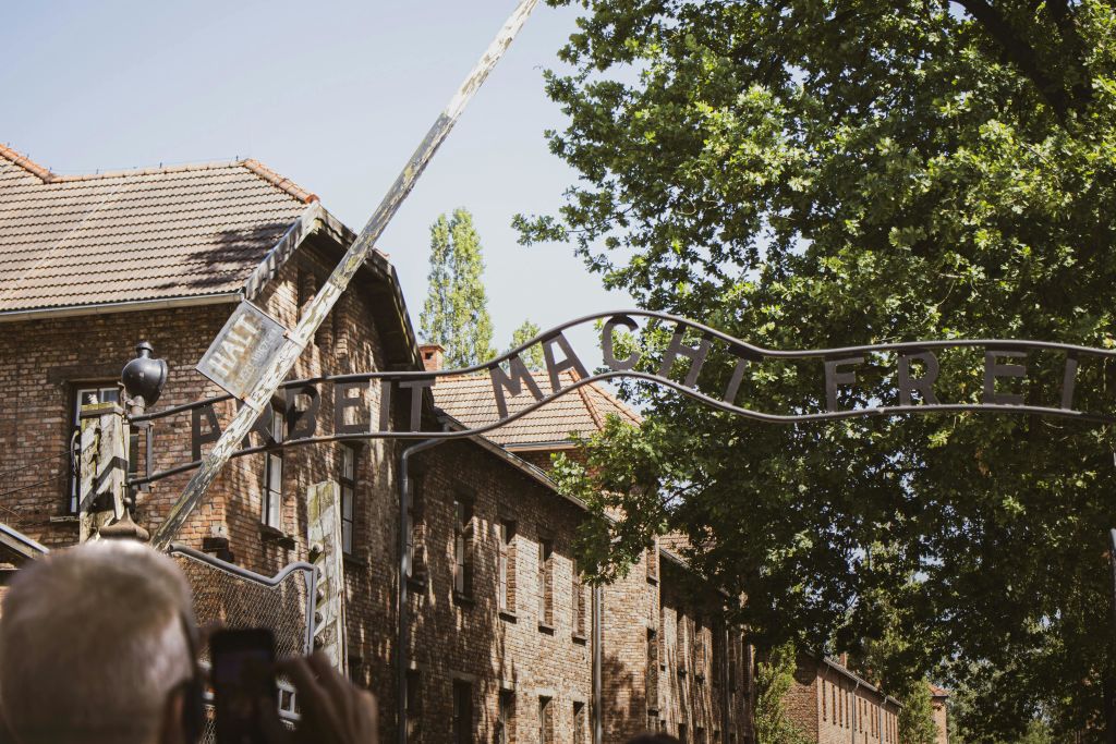 녹지로 둘러싸인 유서 깊은 벽돌 건물 현장에서 "Arbeit macht frei" 레터링이 있는 출입구.