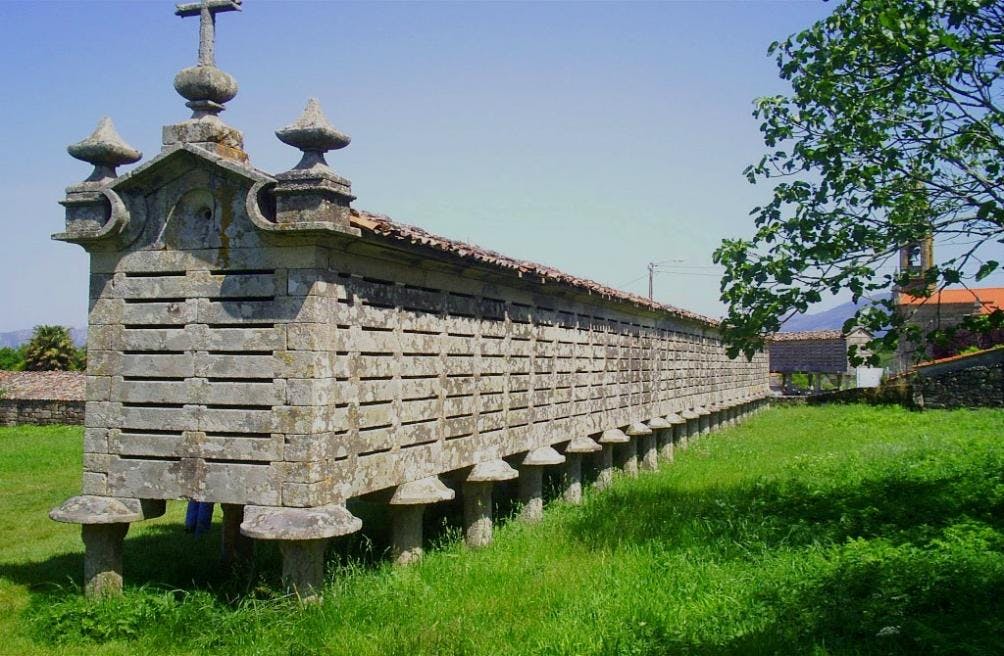 오른쪽에 작은 나무가 있는 맑고 푸른 하늘 아래, 풀밭에 높이 솟은 기둥 위에 길고 오래된 돌로 만든 곡창지대.