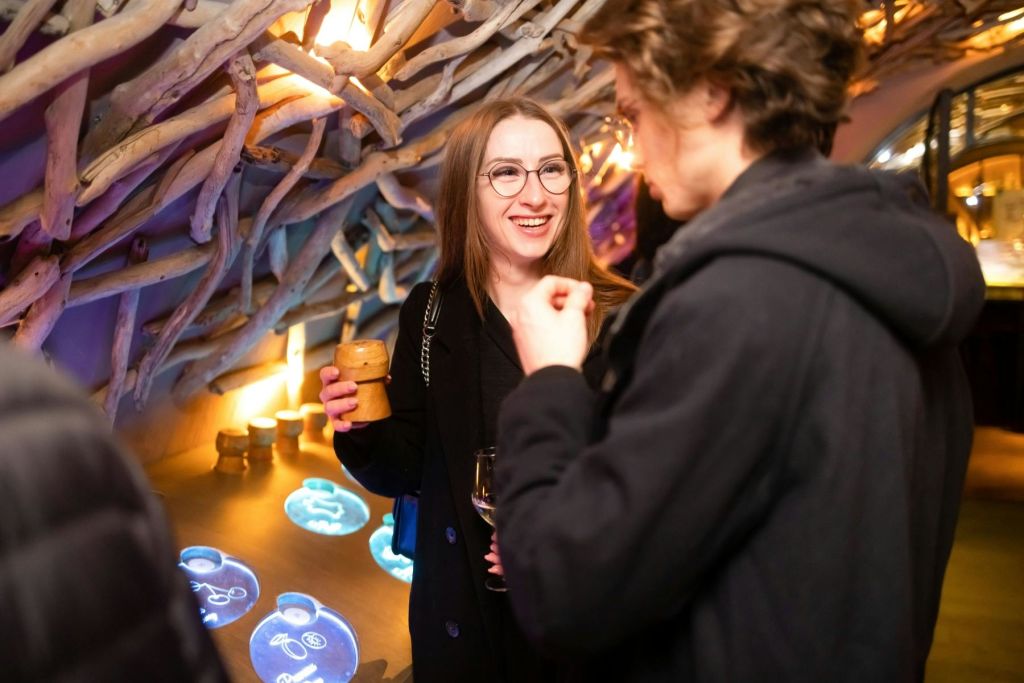 파란색 디스플레이가 빛나는 장식된 장소에서 두 사람이 대화를 나누고 있습니다. 한 사람은 음료를 들고 미소를 짓고 있습니다.