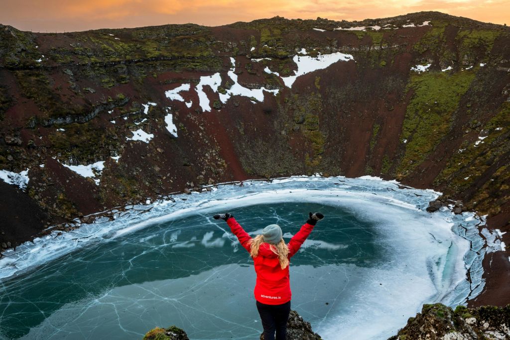 겨울철 분화구가 내려다보이는 바위에 서 있는 사람. 호수가 얼어붙어 있습니다.